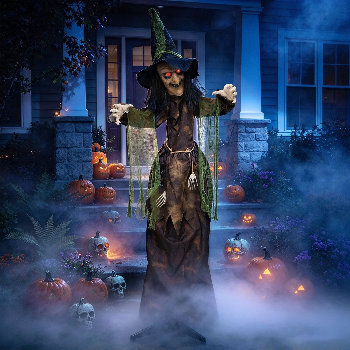 A robed witch decoration with glowing red eyes stands among pumpkins and fog on a porch at night.