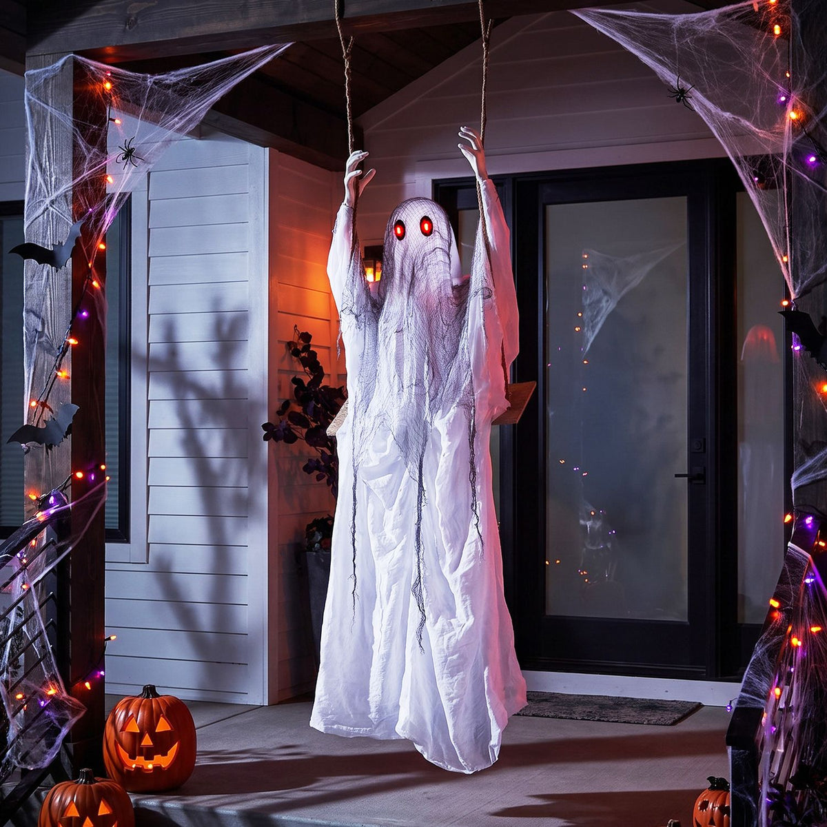 White hanging ghost with red eyes on a decorated porch at night