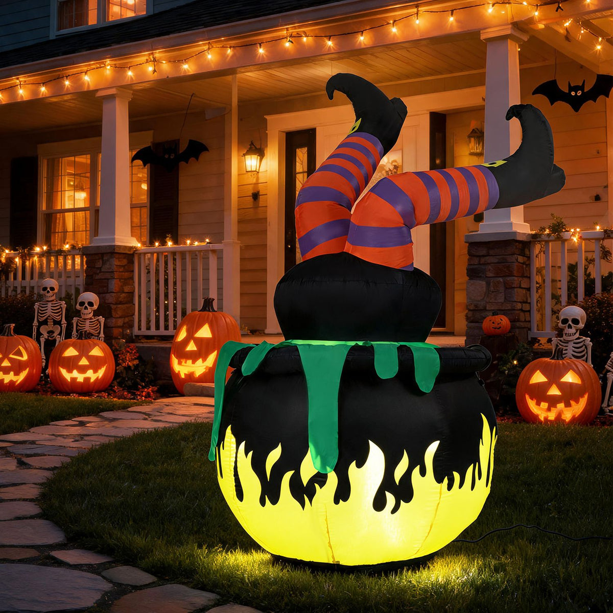 Inflatable witch’s striped legs kick up from a glowing black cauldron on a Halloween-decorated porch.