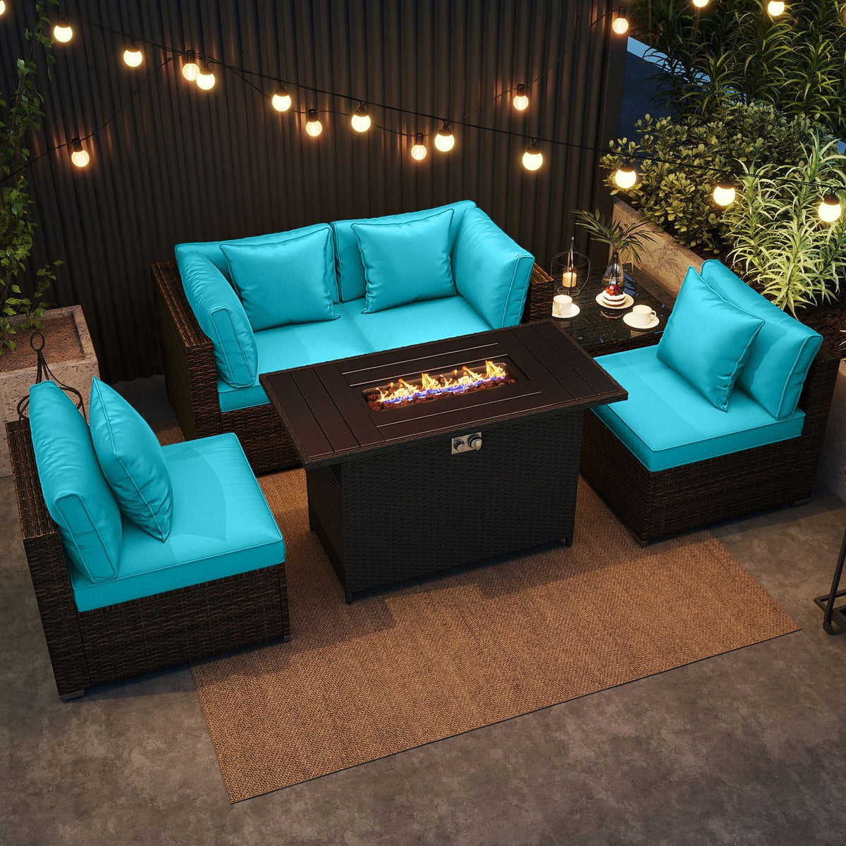 Turquoise patio seating and a lit fire pit table arranged on a rug beneath warm string lights.
