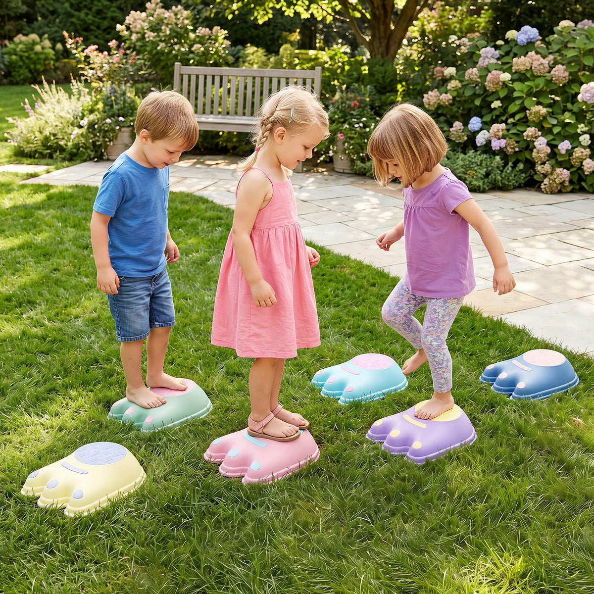 Three children step across colorful monster-shaped stones on a garden lawn.