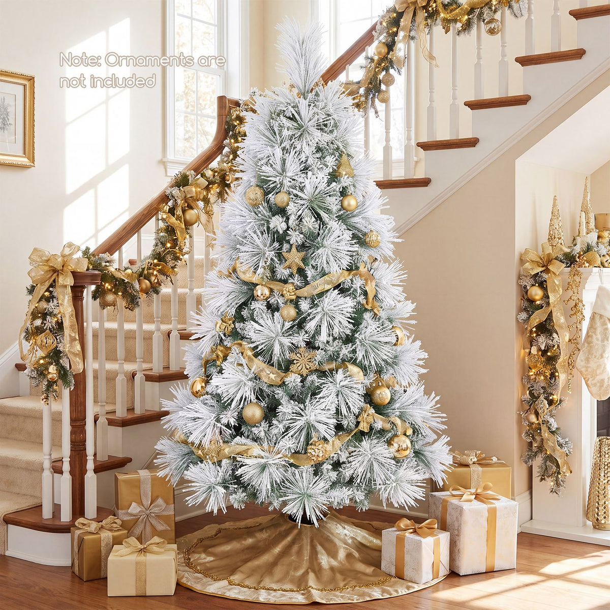Flocked Christmas tree with glowing lights and gold decorations beside a decorated staircase and wrapped gifts.