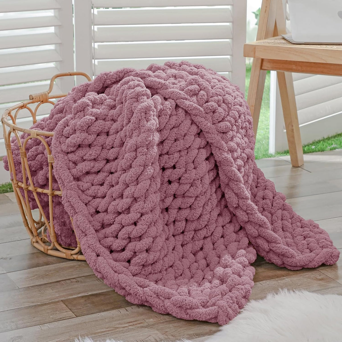 Dusty pink chunky chenille throw with thick rope-knit draped from a woven basket onto a wood floor.