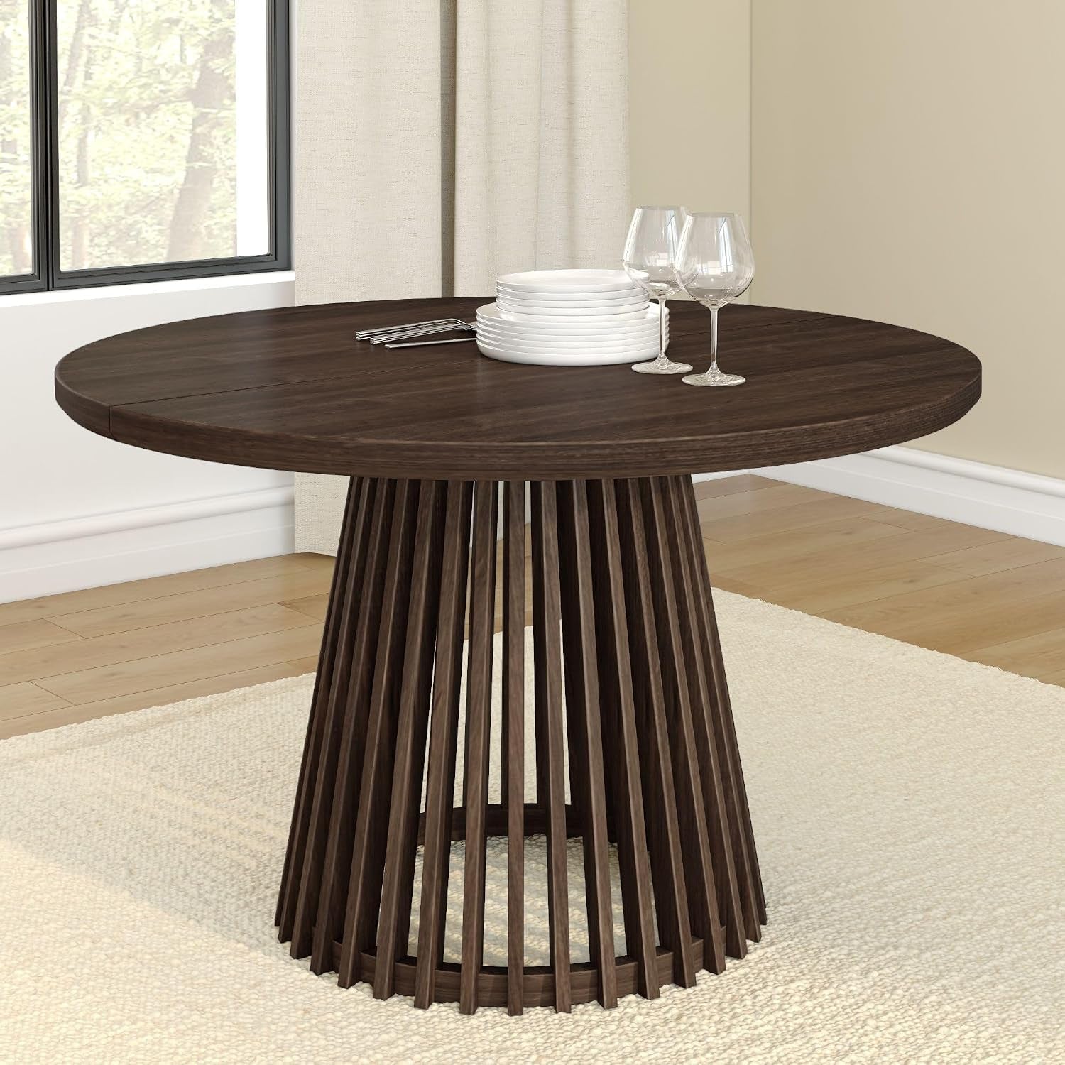 Round deep brown wood dining table with slatted pedestal base shown with glassware.