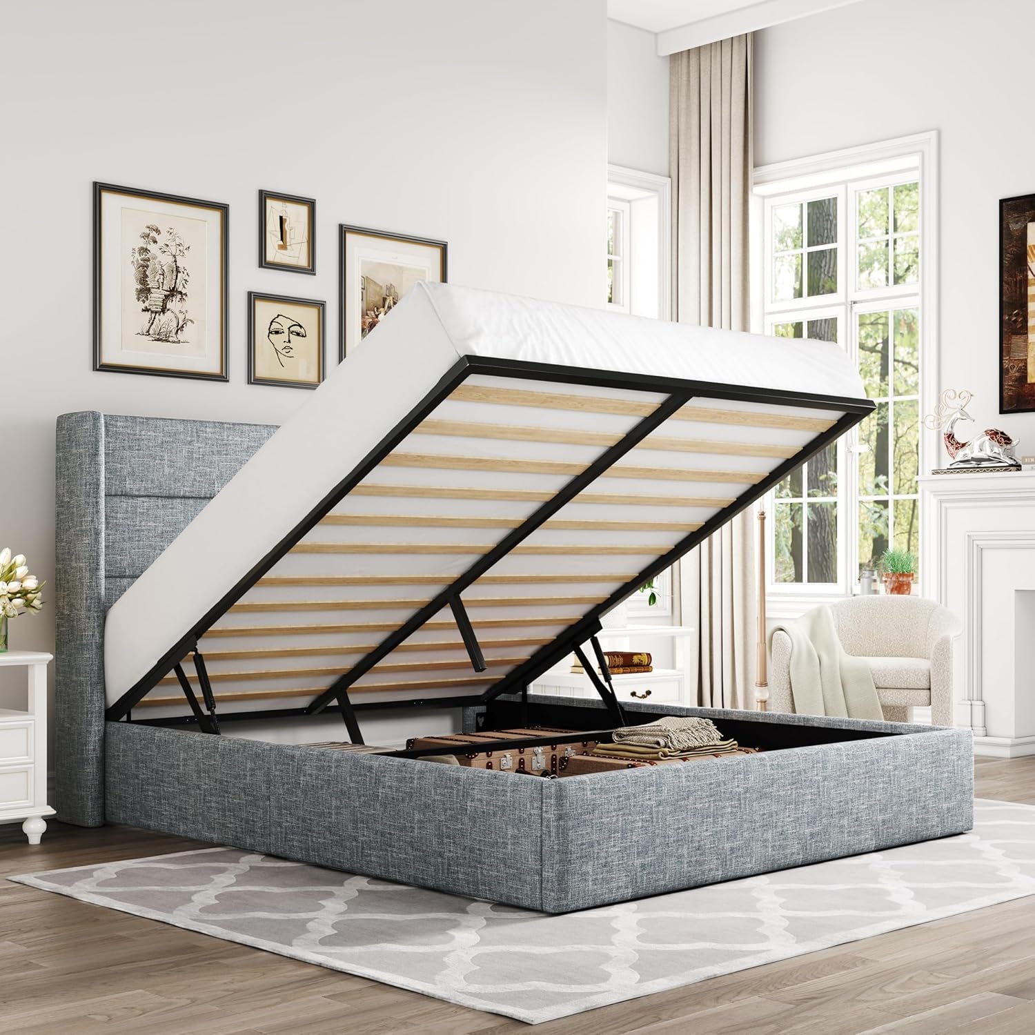 Bedroom scene showing a gray upholstered storage bed with the mattress lifted to reveal open underbed storage in a staged