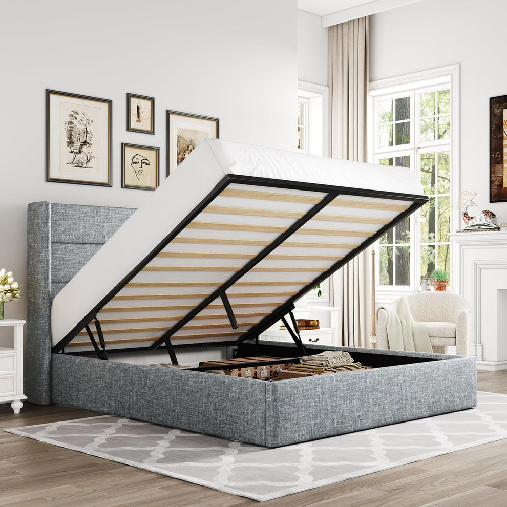 Bedroom scene showing a gray upholstered storage bed with the mattress lifted to reveal open underbed storage in a staged