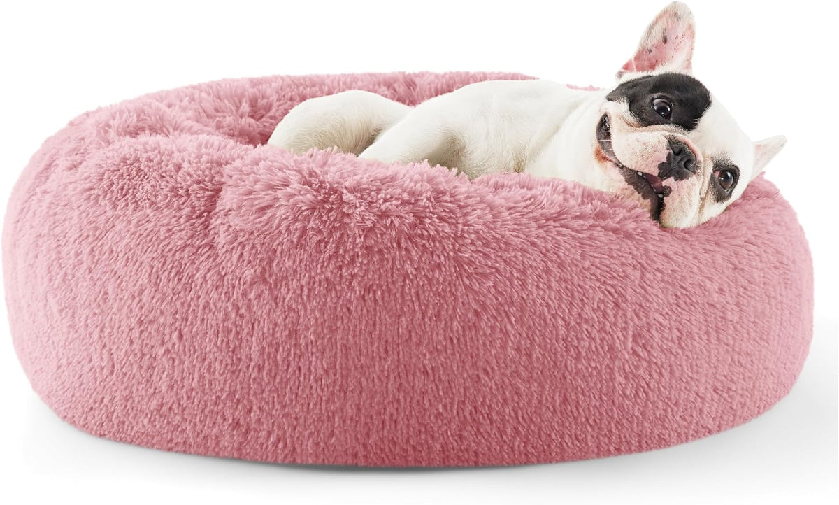 White and black-faced dog lying in a pink round faux-fur donut bed, shown from the side.