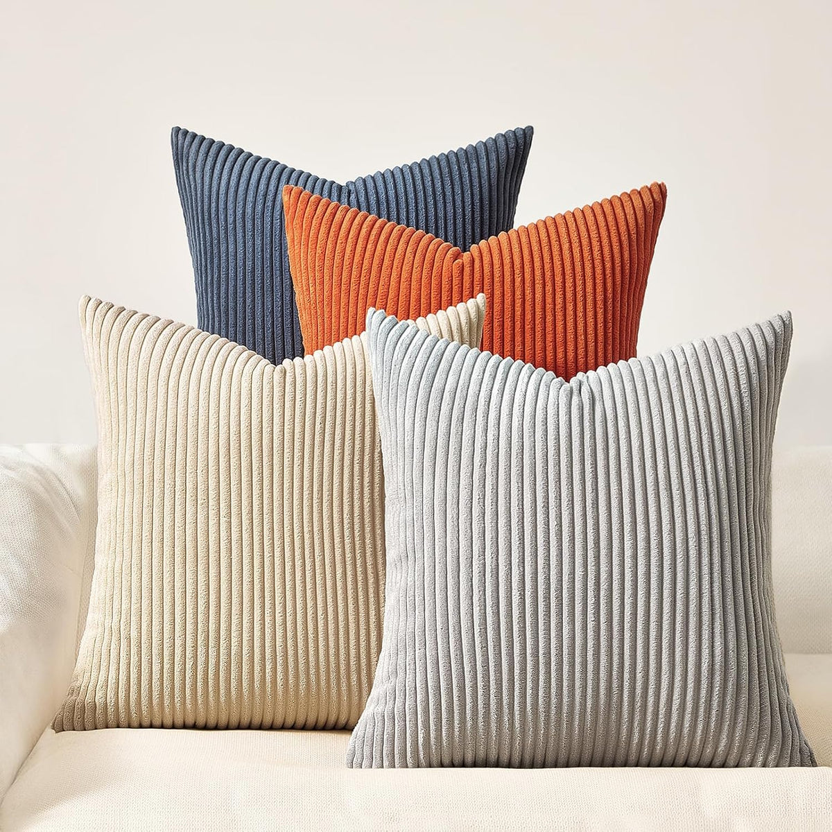 Five ribbed corduroy pillows in cream, light gray, blue, burnt orange and navy arranged on a sofa