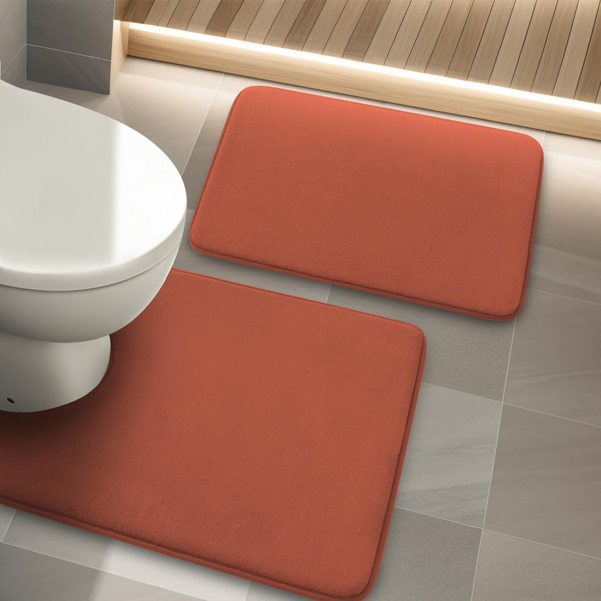Top-down view of two terracotta memory-foam bath mats placed on gray tile next to a white toilet.
