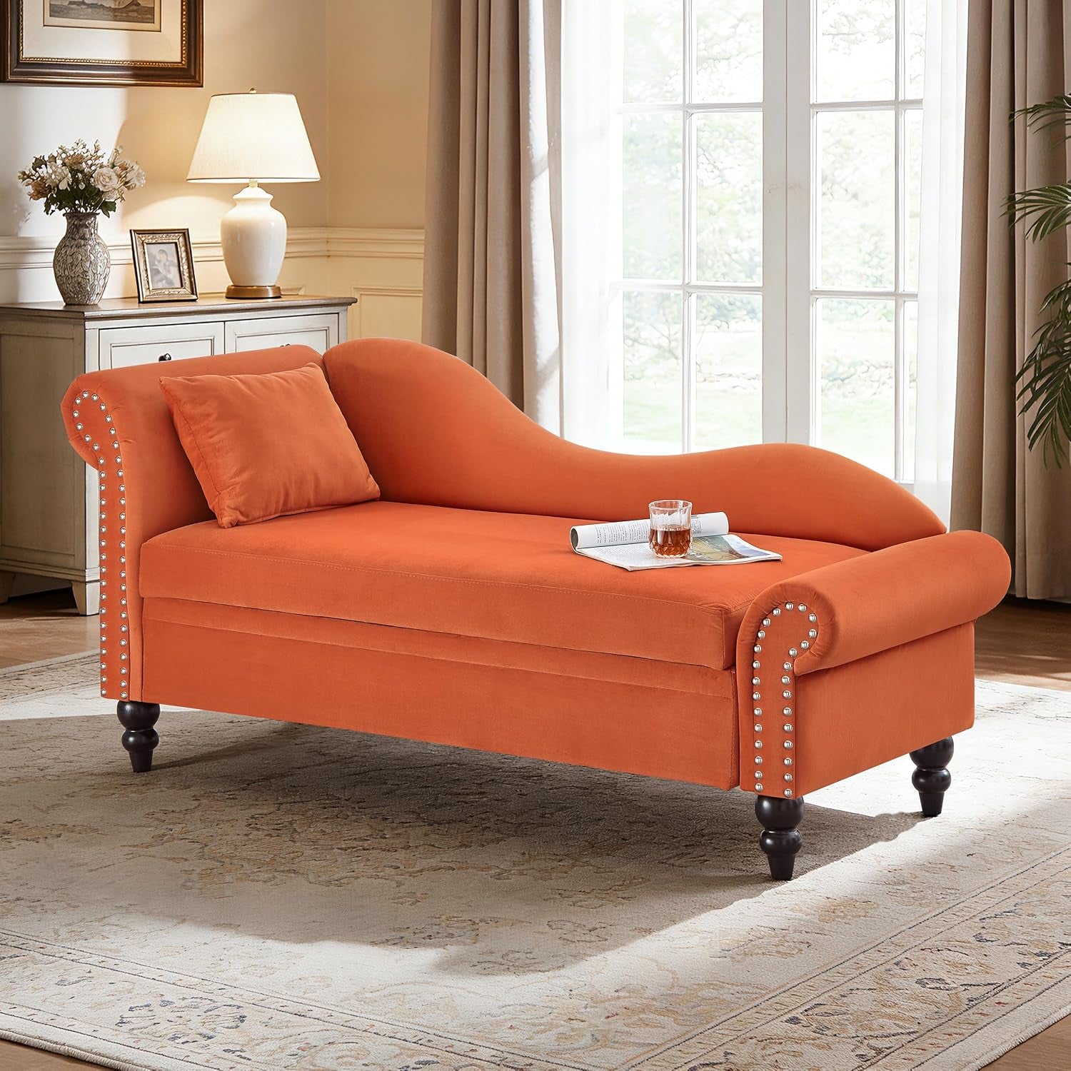 Three-quarter view of a right-facing burnt-orange chaise with turned dark legs, studded trim, pillow and a drink on the seat