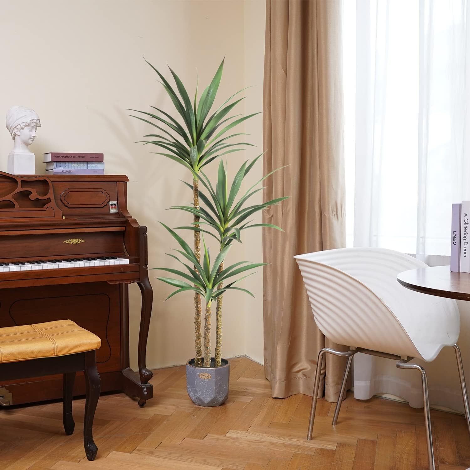 Artificial agave placed between an upright wooden piano and a white modern dining chair by beige curtains.