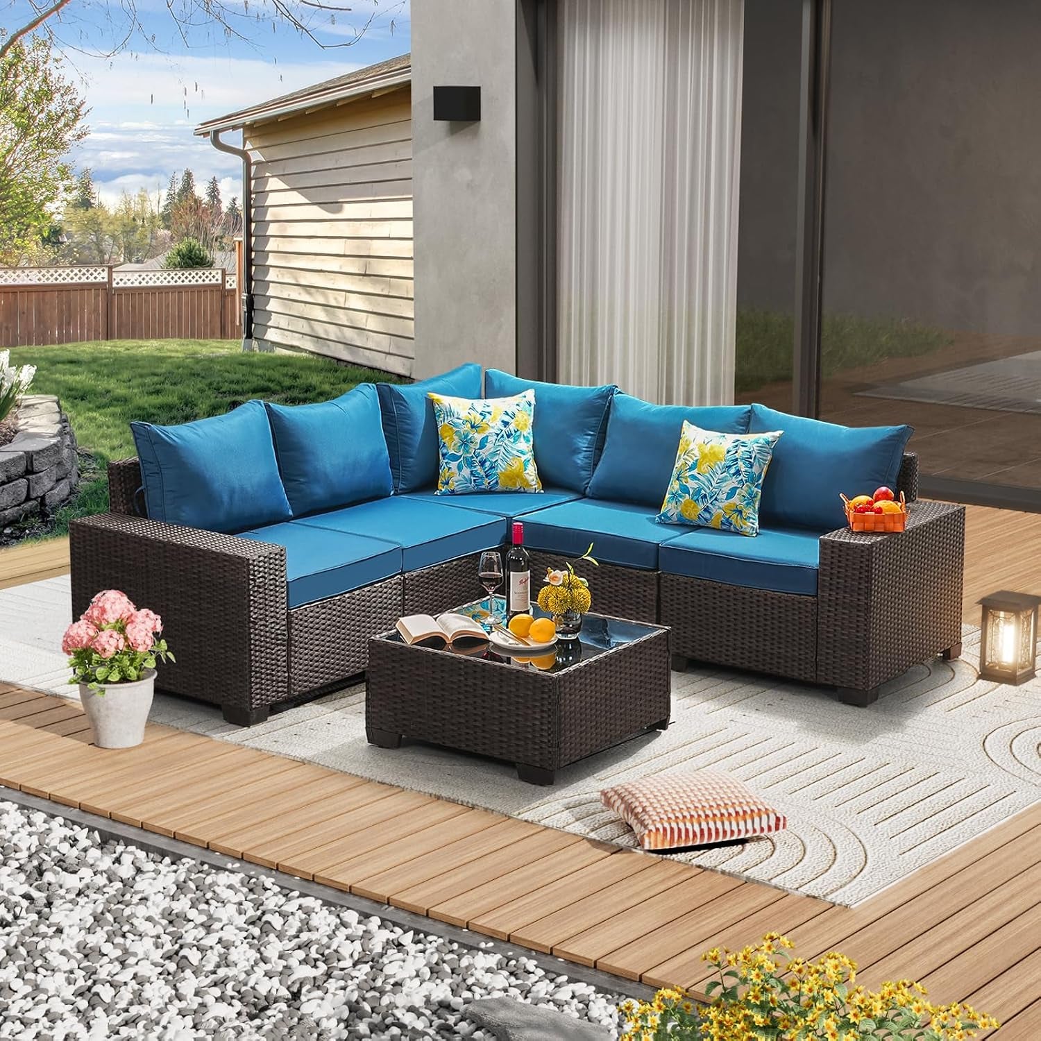 Corner view of the dark rattan sectional with bright teal cushions and patterned throw pillows beside a glass coffee table.