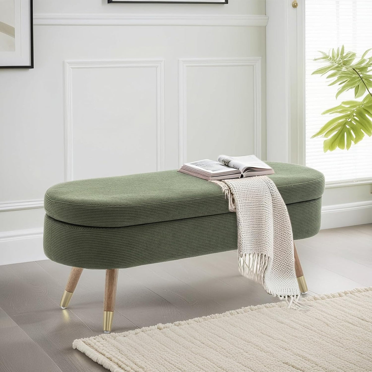 Olive green oval bench with wooden legs and gold feet beside a window, styled with a book and throw.