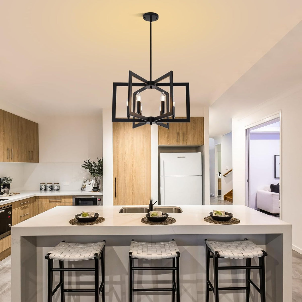 Kitchen island with a black geometric six-light chandelier hanging above a white countertop and three bar stools.