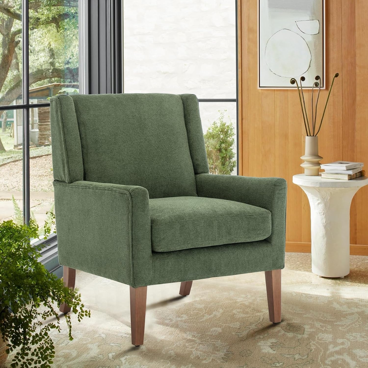 Green chenille wingback chair with wooden legs beside a side table in a sunlit room
