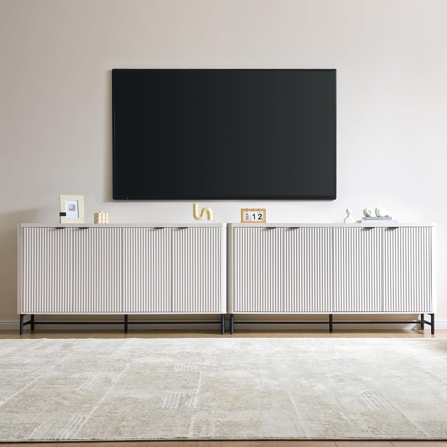 Wide shot of a low white ribbed buffet under a wall-mounted TV, decorative objects on top.