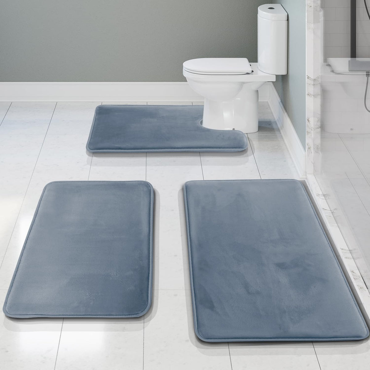 Stone blue rectangular bath mats and contour mat arranged on white tile, front view