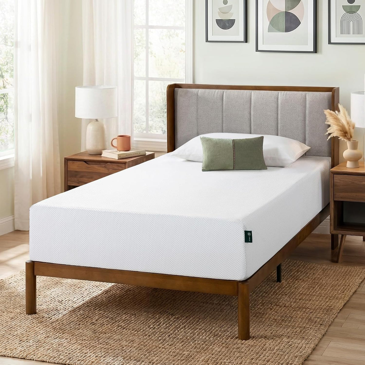 Angled view of a white mattress on a mid-century wooden bed frame over a woven rug