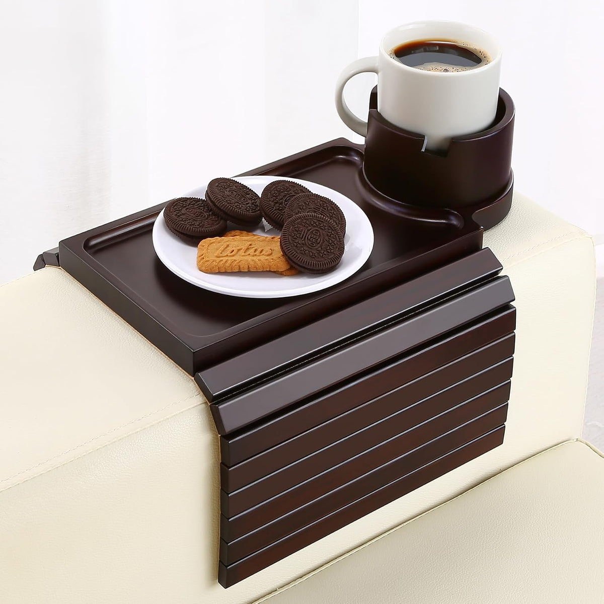 Dark brown slatted bamboo arm tray on a cream sofa arm with a plate of cookies and a mug in the rotating cup holder.