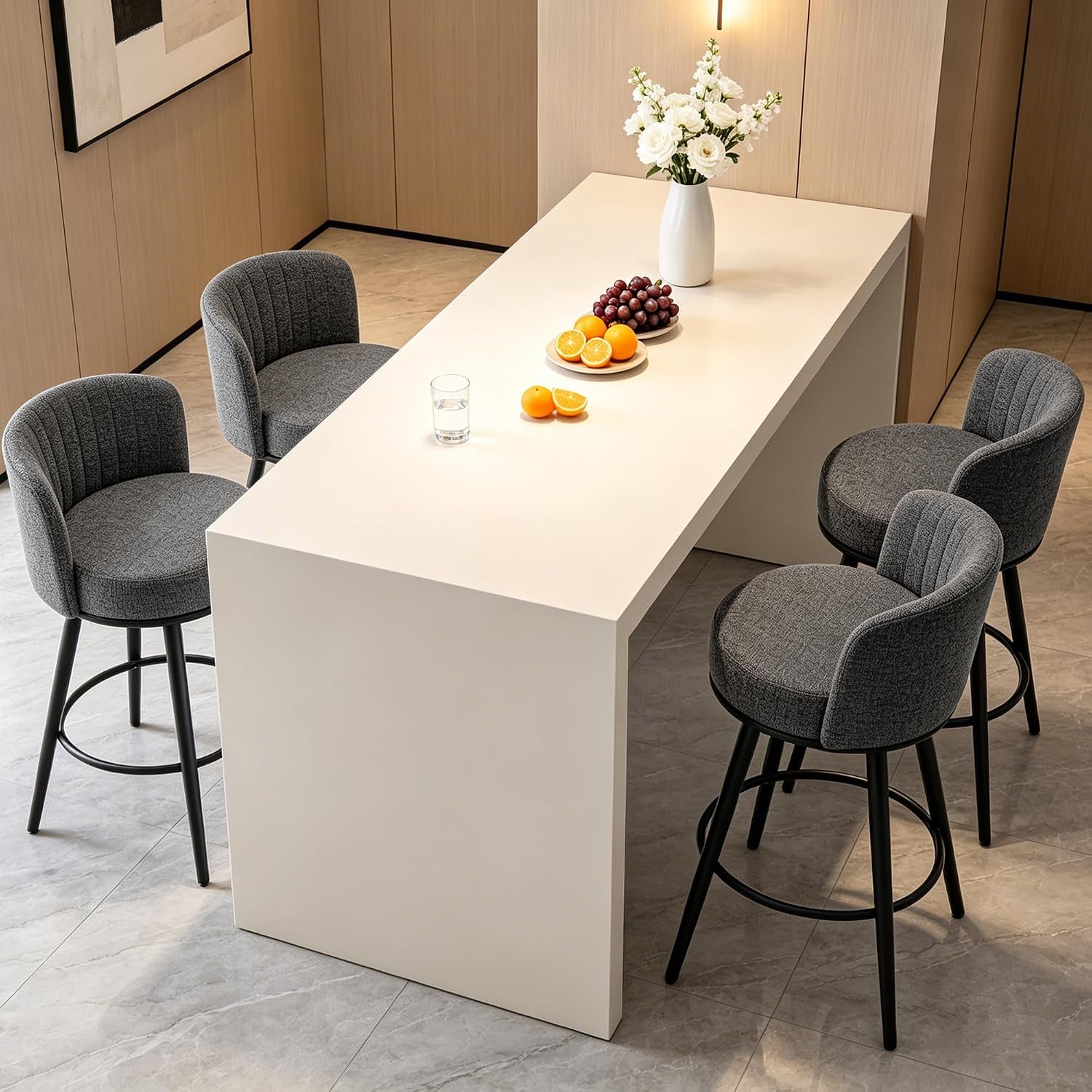 Angled view of four dark-gray swivel stools along a tall white island topped with fruit and a vase