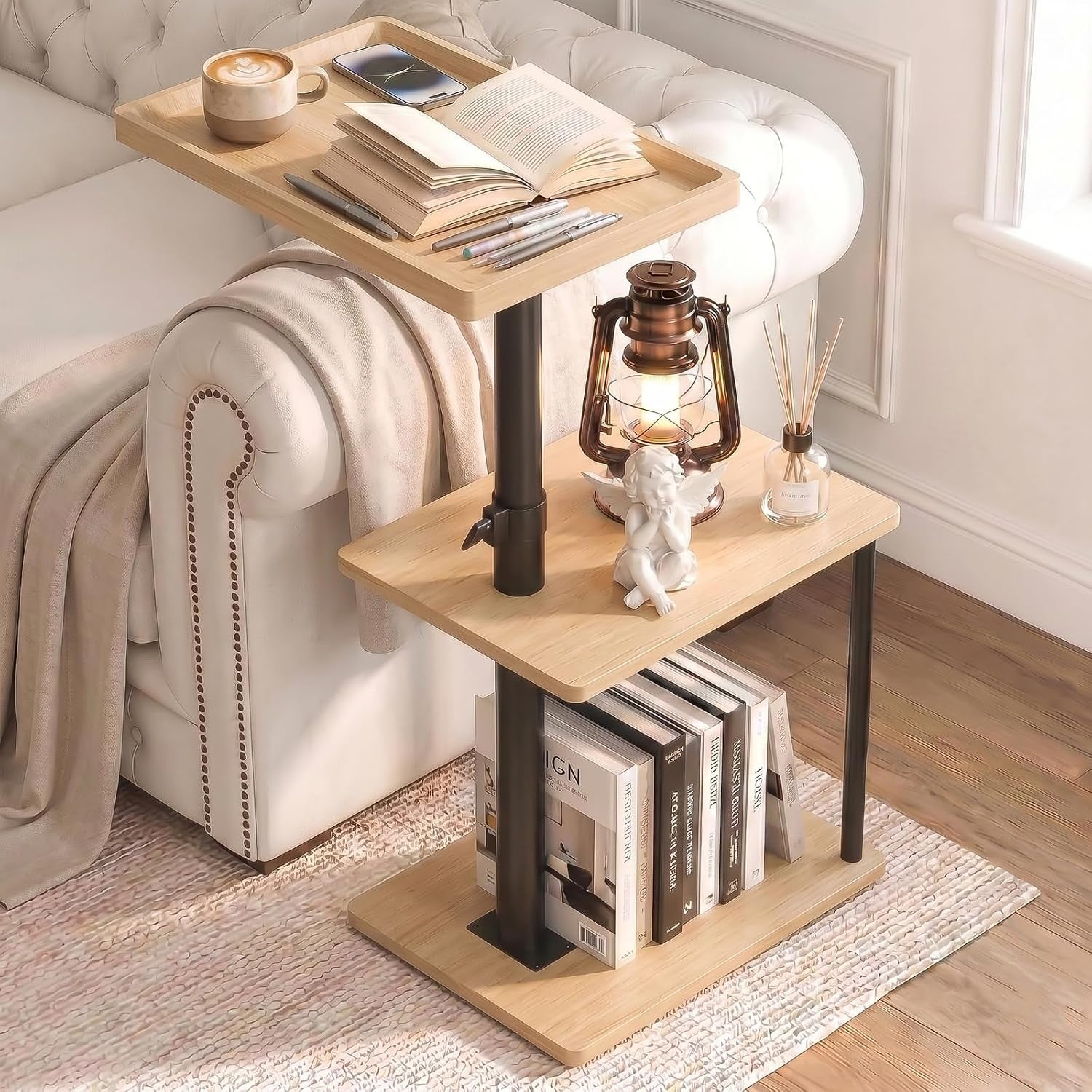 Light wood three-tier C-table with black post and books on the bottom shelf next to a tufted sofa