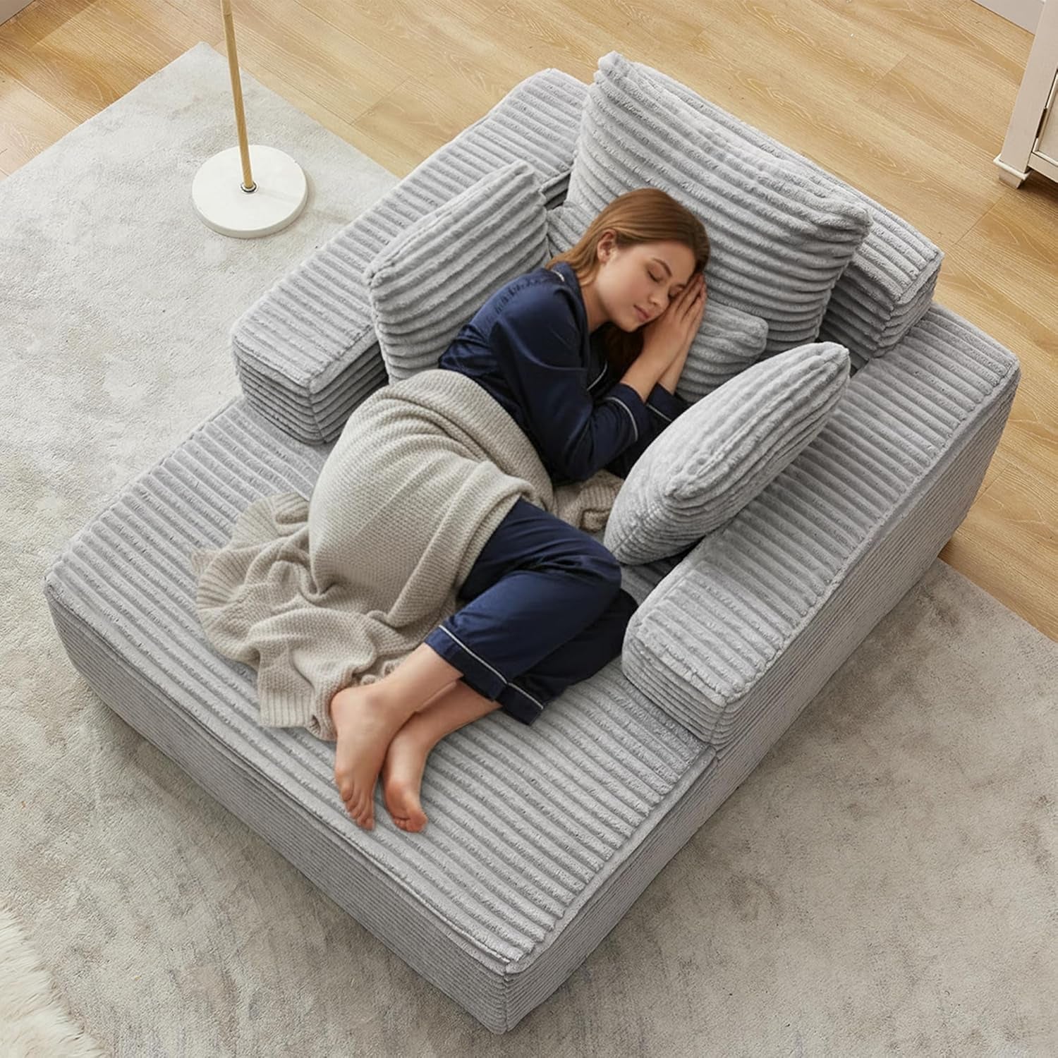 Top-down view of a light gray corduroy chaise with ribbed cushions and a woman sleeping with a blanket.