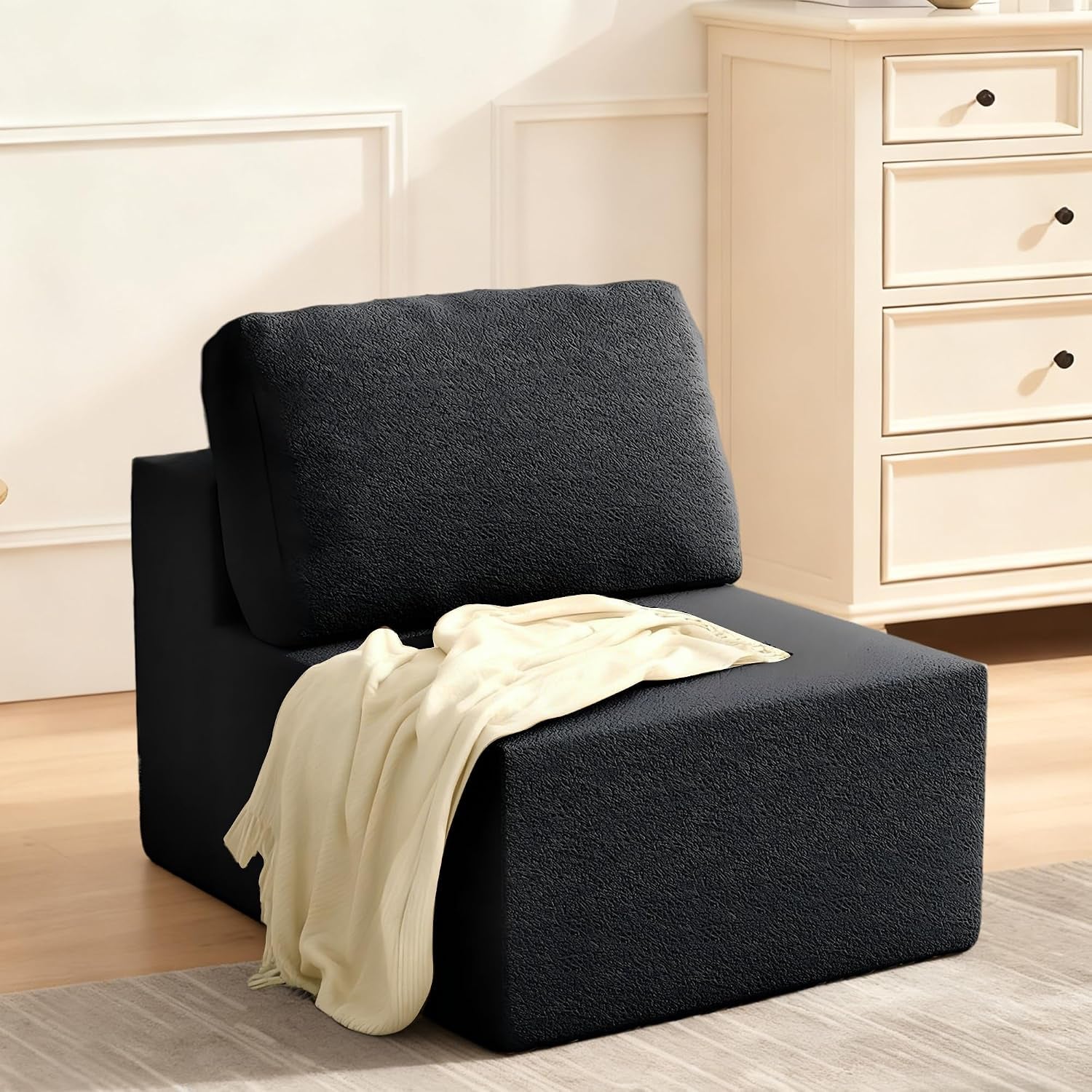 Single black modular seat with back cushion and a light throw draped over it in a room corner.