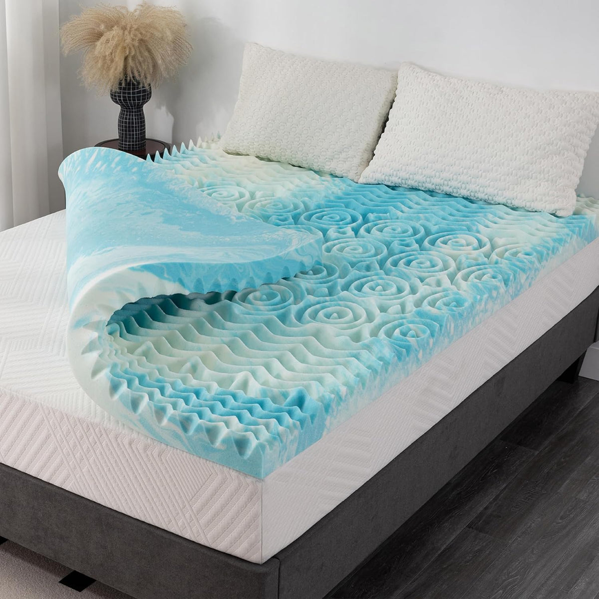 Blue-and-white egg crate gel memory foam topper folded back on a mattress with two white pillows and bedside decor