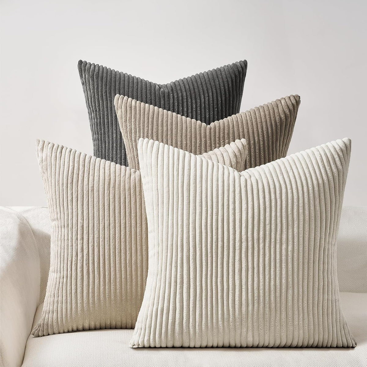 Set of four ribbed corduroy square pillows in shades of gray and beige arranged on a sofa.