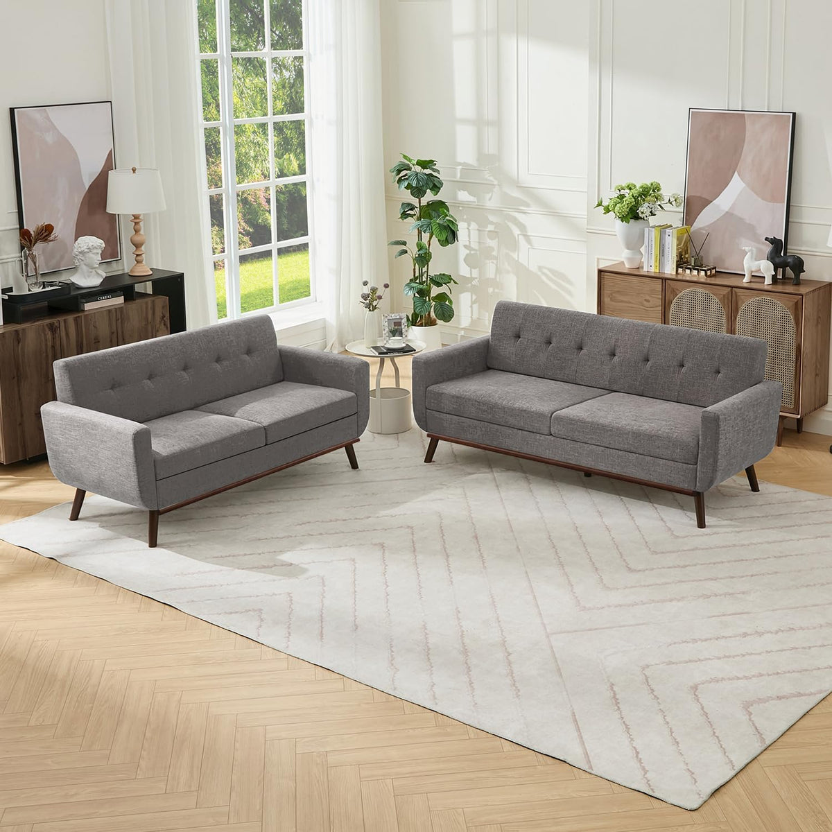 Two gray mid-century sofas staged in a sunlit room on a large area rug, side table between them.