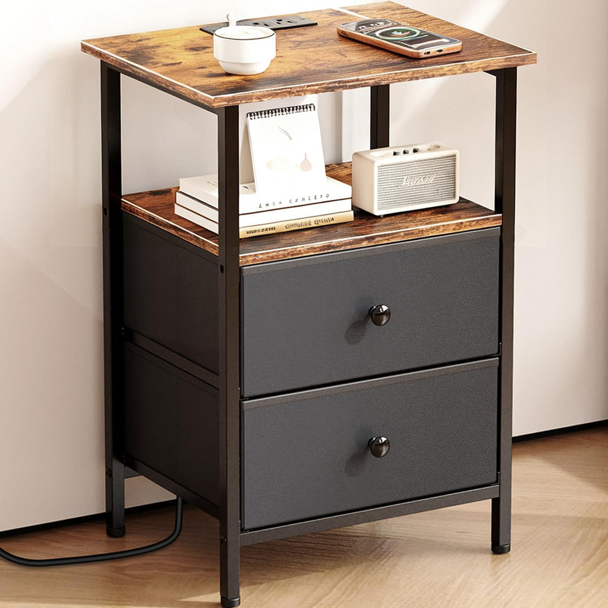 Front three-quarter view of a nightstand with wood top, open shelf and two dark fabric drawers in a black metal frame.