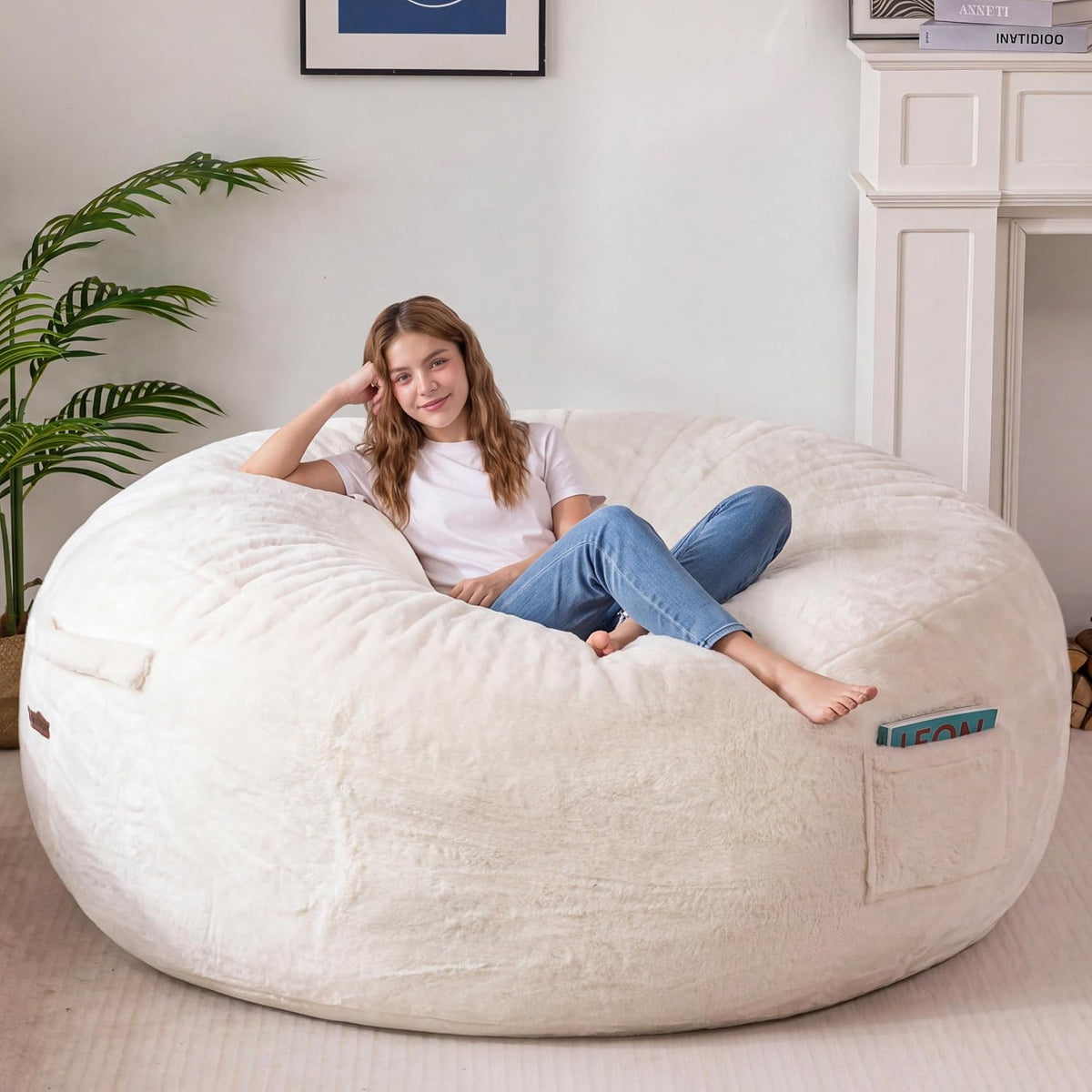 Woman lounging on a cream/ivory faux‑fur bean bag, legs stretched and a book tucked into the side pocket.
