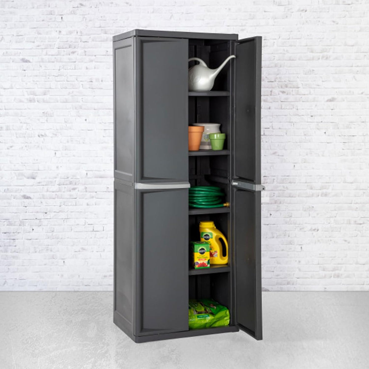 Gray storage cabinet with one door open against a white brick wall showing a garden hose, pots, and containers on four inside