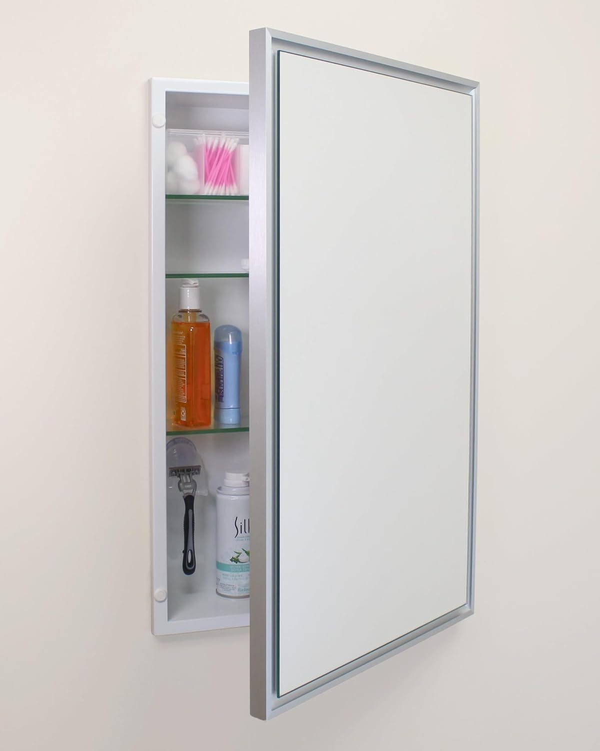 Recessed medicine cabinet with silver metal frame, mirrored door open to reveal three glass shelves and toiletries.