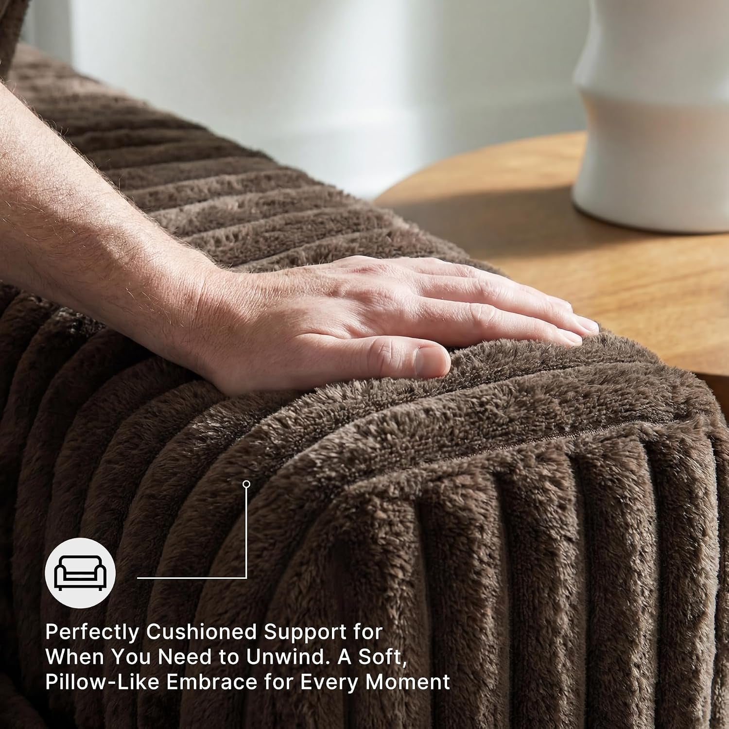Close-up of a hand resting on ribbed chocolate-brown corduroy armrest with a wooden side table blurred background.