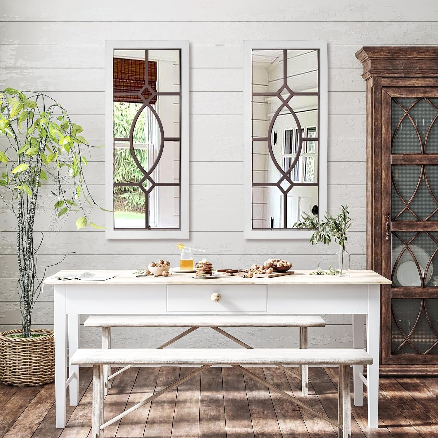 Two narrow vertical mirrors hung side-by-side above a farmhouse table and bench set with breakfast items.
