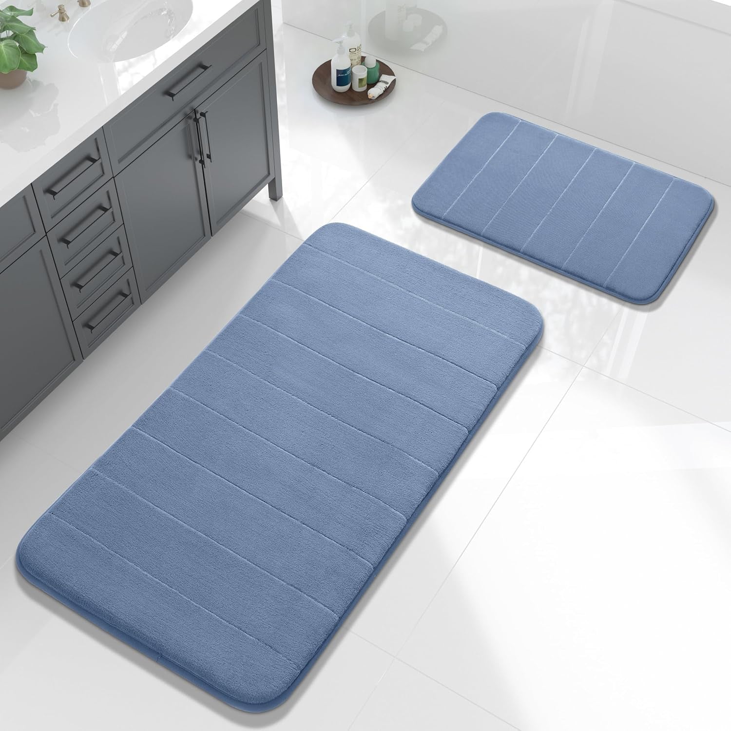 Overhead view of a large and small blue rectangular bath mats on a shiny bathroom floor near a sink cabinet.