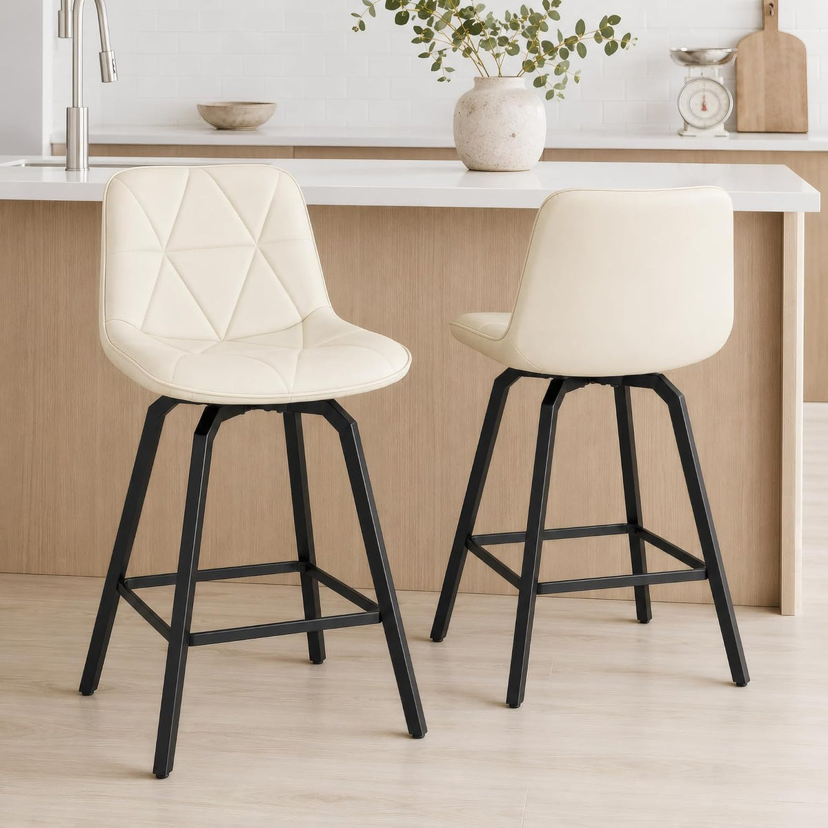 Two white counter stools shown front and back, quilted seat fronts and smooth backs with black metal legs and footrests.