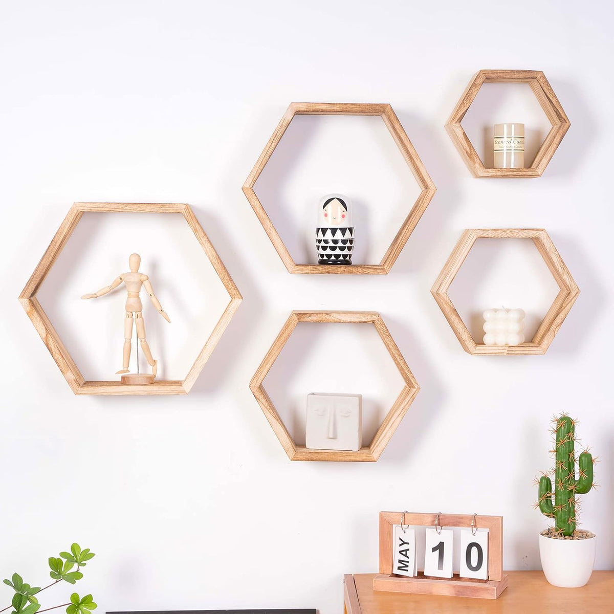 Styled wall vignette with five driftwood-finish hex shelves holding small decor and a potted plant