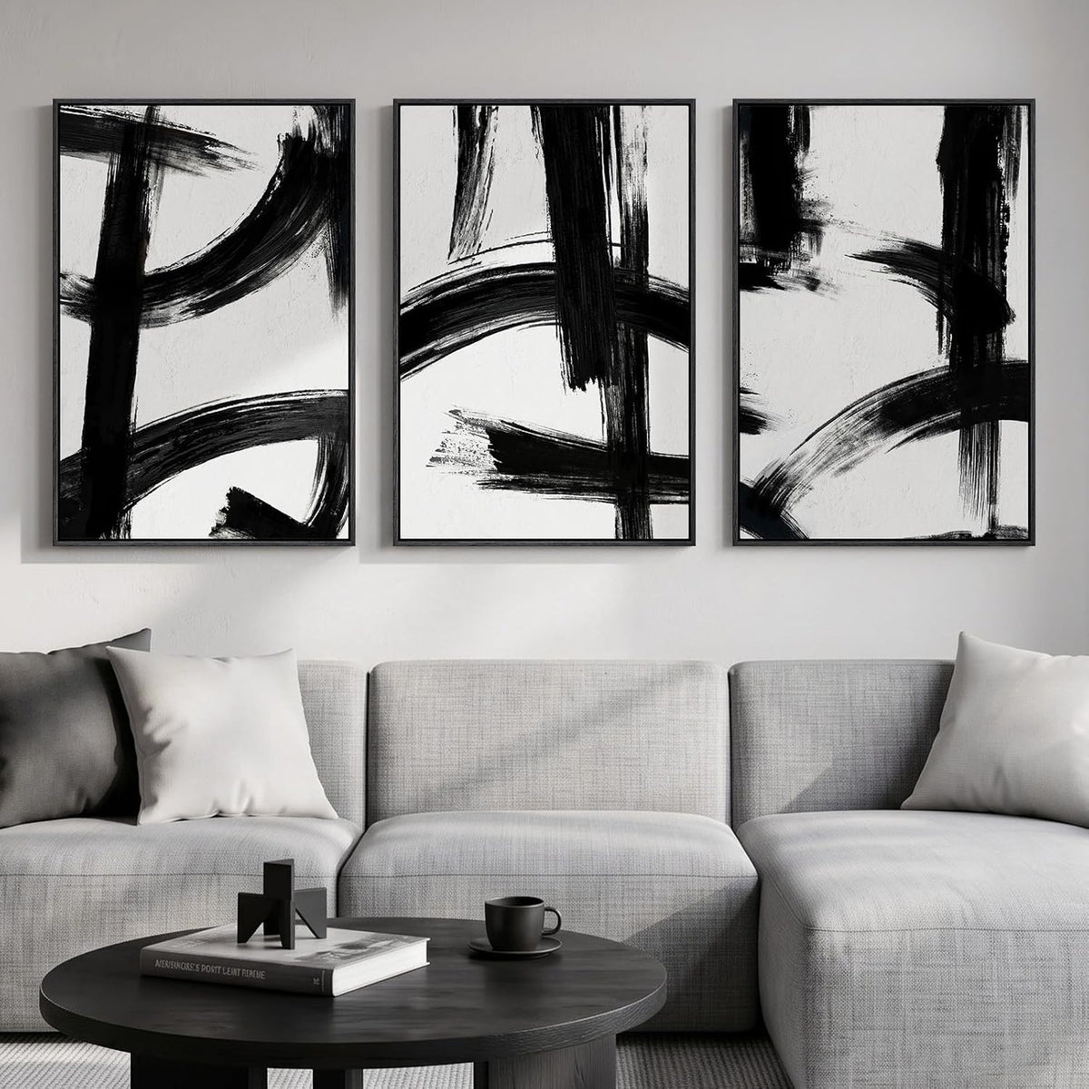Three vertical framed panels with bold black brushstrokes above a light gray sectional and round black coffee table.