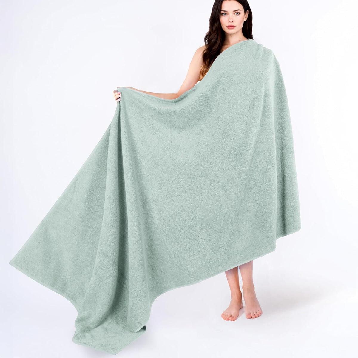 Woman barefoot holding open a large pale mint-green towel draped across her shoulders