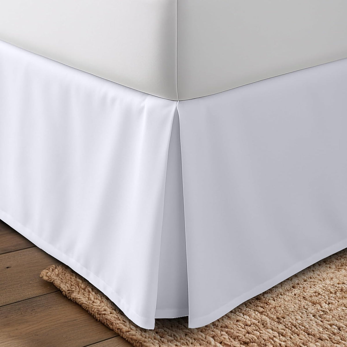 Close-up corner view of a white pleated bed skirt hanging from a mattress corner