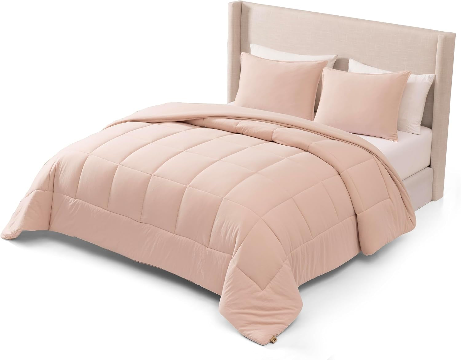 Angled view of a made bed with a soft blush/pale pink box‑stitched comforter and two matching shams.