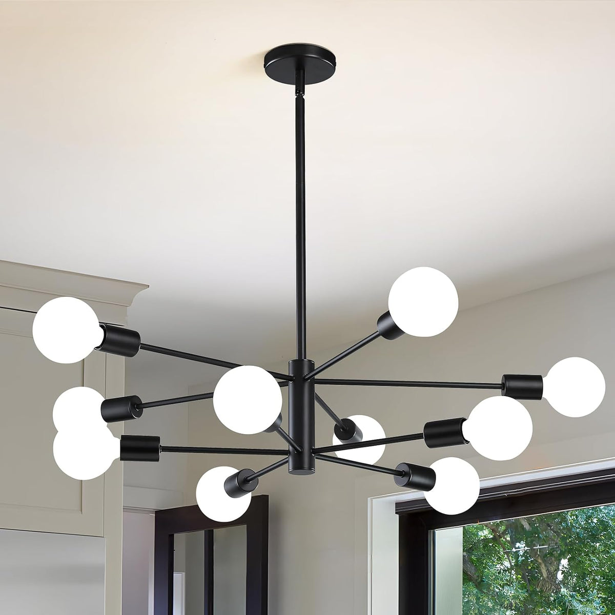 Matte black modern chandelier with twelve lit globe bulbs hanging above a doorway and window.