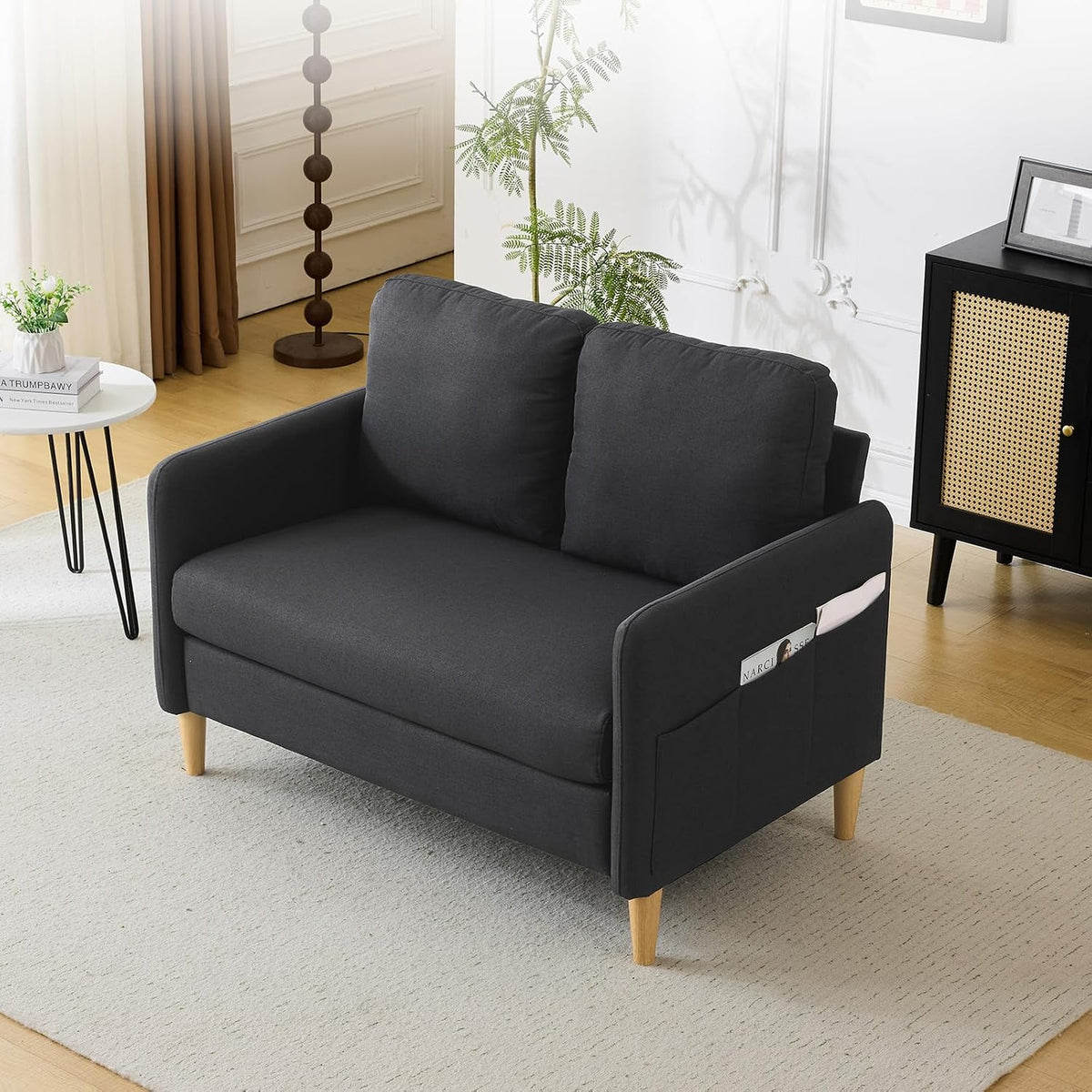 Dark-gray loveseat in a bright room with magazine in side pocket and decorative cabinet nearby