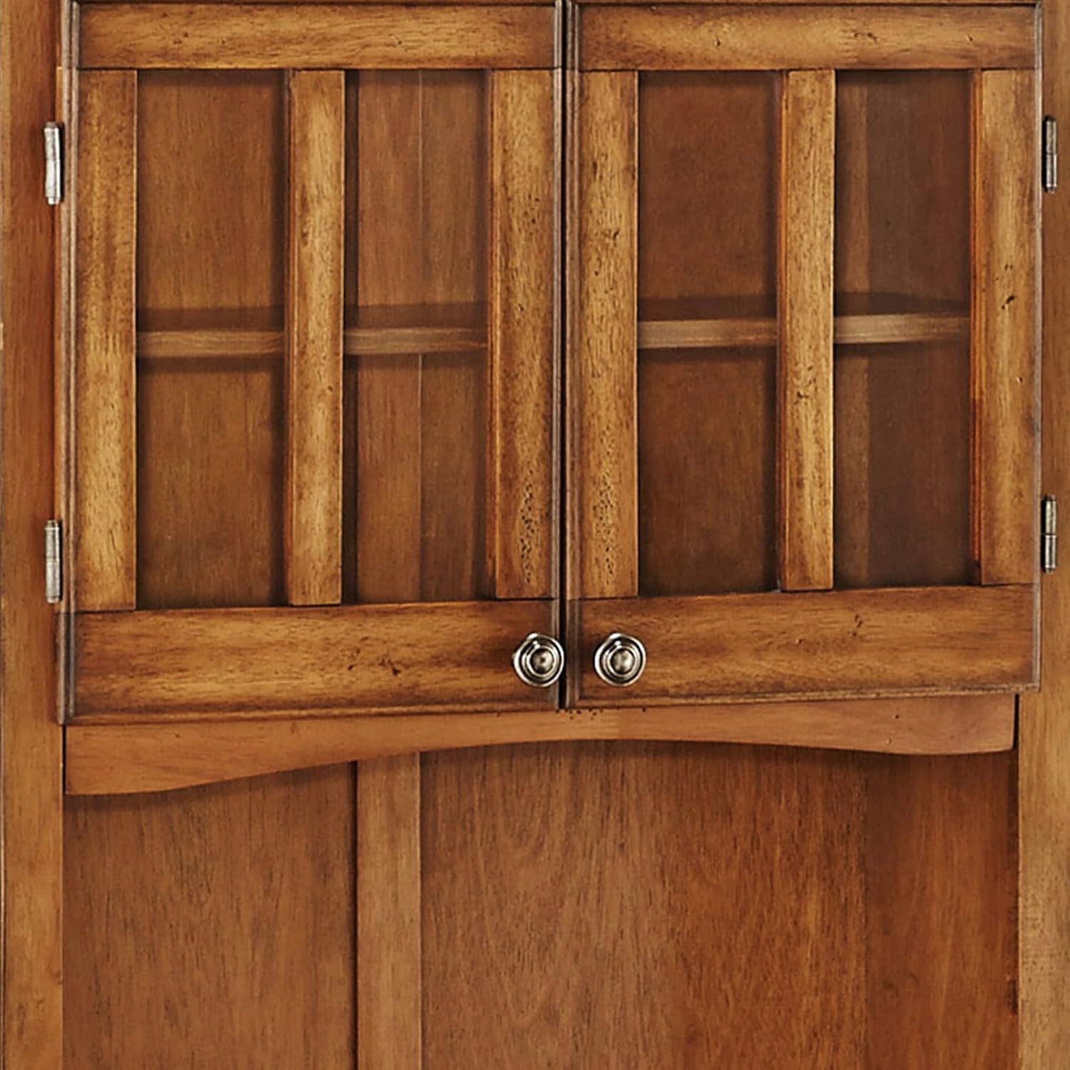 Close-up of wood-framed glass hutch doors and round brushed steel knobs in cottage oak finish