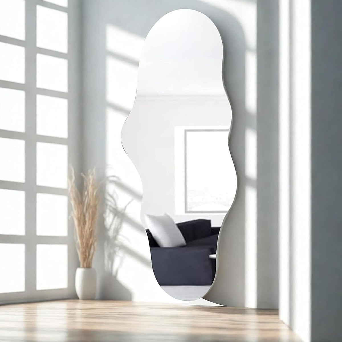 Cloud-shaped frameless mirror leaning against a white wall with strong window grid shadows and a sofa reflected in the glass