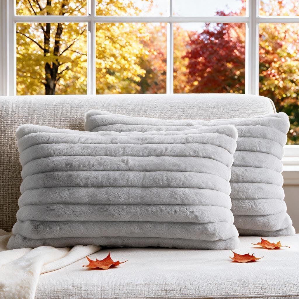 Two cream-white ribbed faux-fur rectangular pillow covers on a beige sofa with autumn leaves and a window behind.