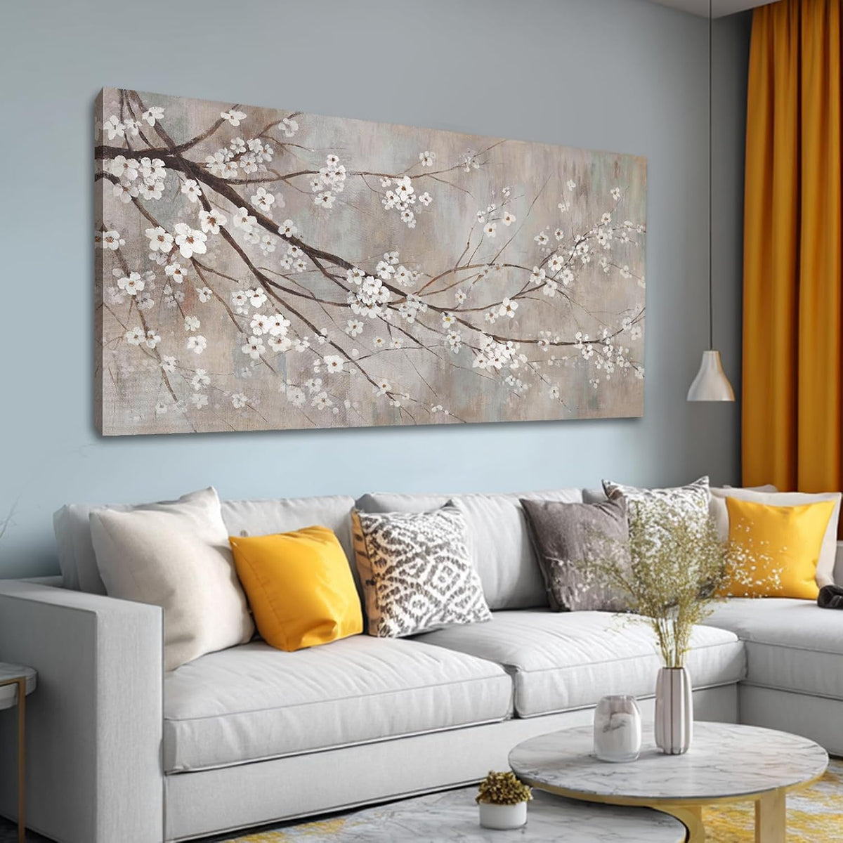 Angled view of plum-blossom canvas on a pale blue wall above a gray sectional, mustard curtains at right