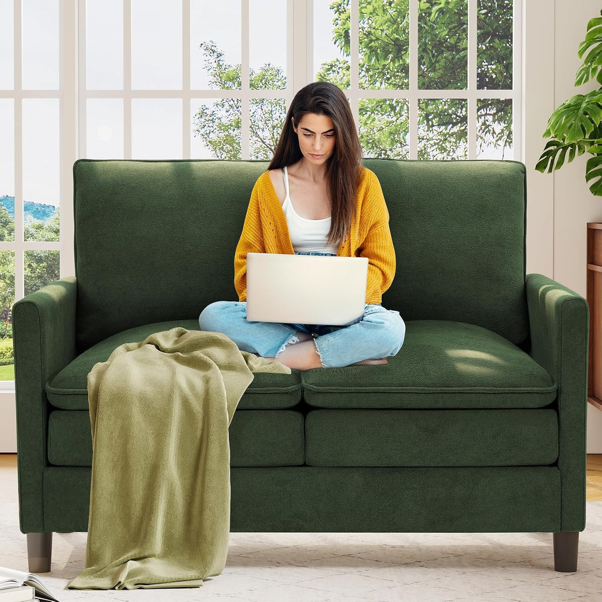 Woman using a laptop seated cross-legged on a dark green small loveseat